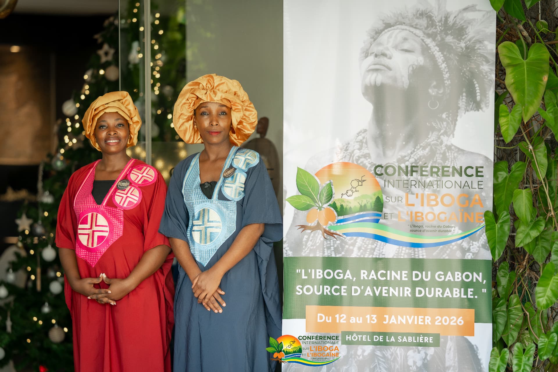 Conference hosts in traditional Gabonese dress beside the event banner